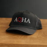 Black performance cap with embroidered 'AQHA' logo on a wooden surface