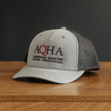 Gray cap with a black mesh back with embroidered AQHA logo on a wooden surface